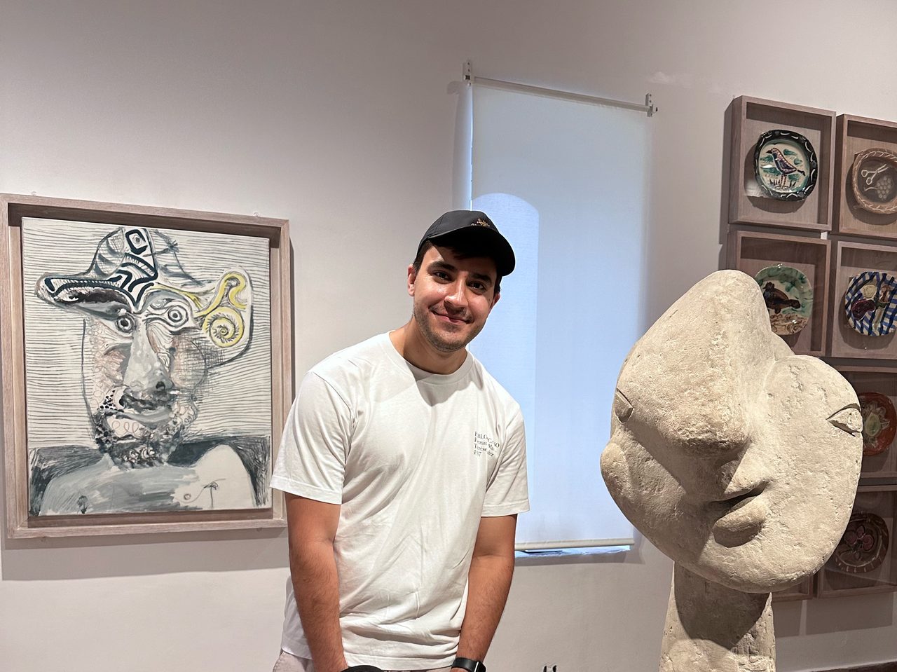 Sam, smiling, in a museum gallery beside a large stone sculpture of a head and a painted portrait.